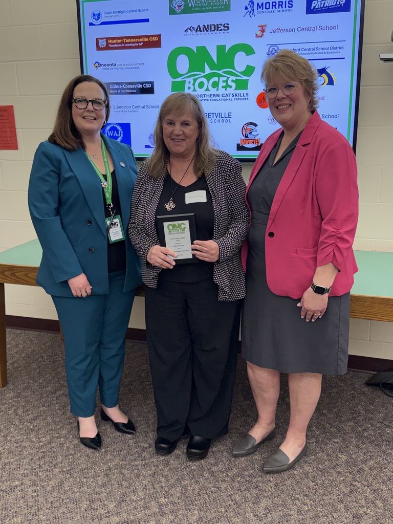 ONC District Superintendent, Laurie Sweeney who received an award, and the Director of Student Programs posing in front of a screen with the ONC logo along with the logos of the 19 component districts. Laurie is holding her award.