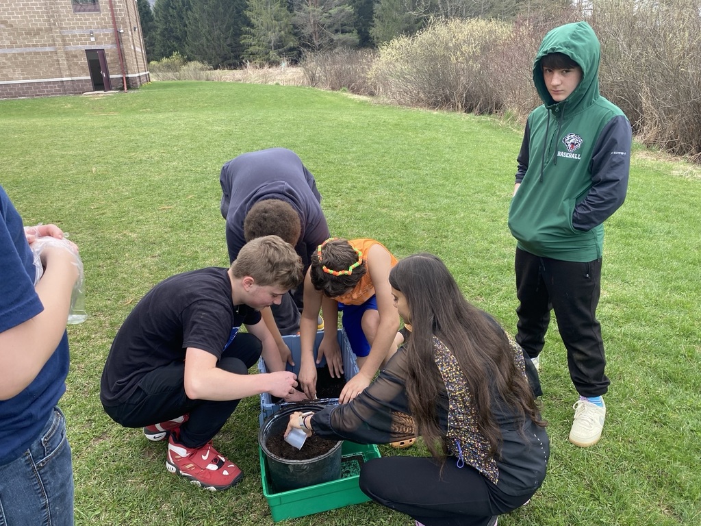 Four students crouching and digging in buckets of dirt planting. One student standing and watching.