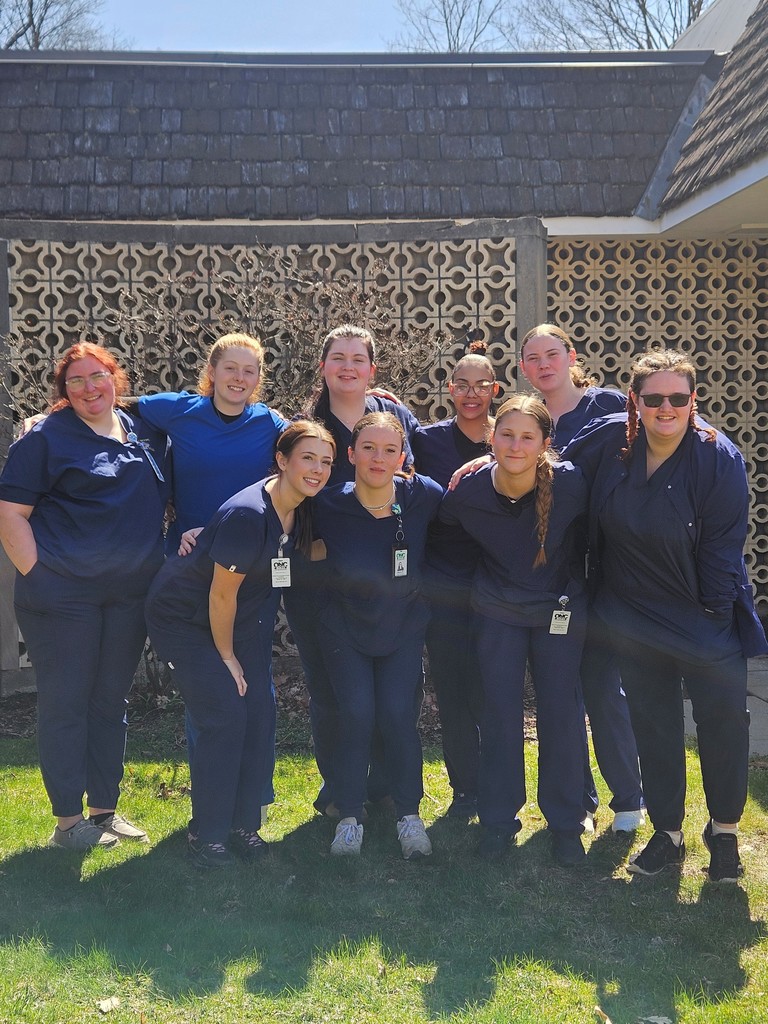 9 Health Occuapations students in scrubs posing for a picture outside
