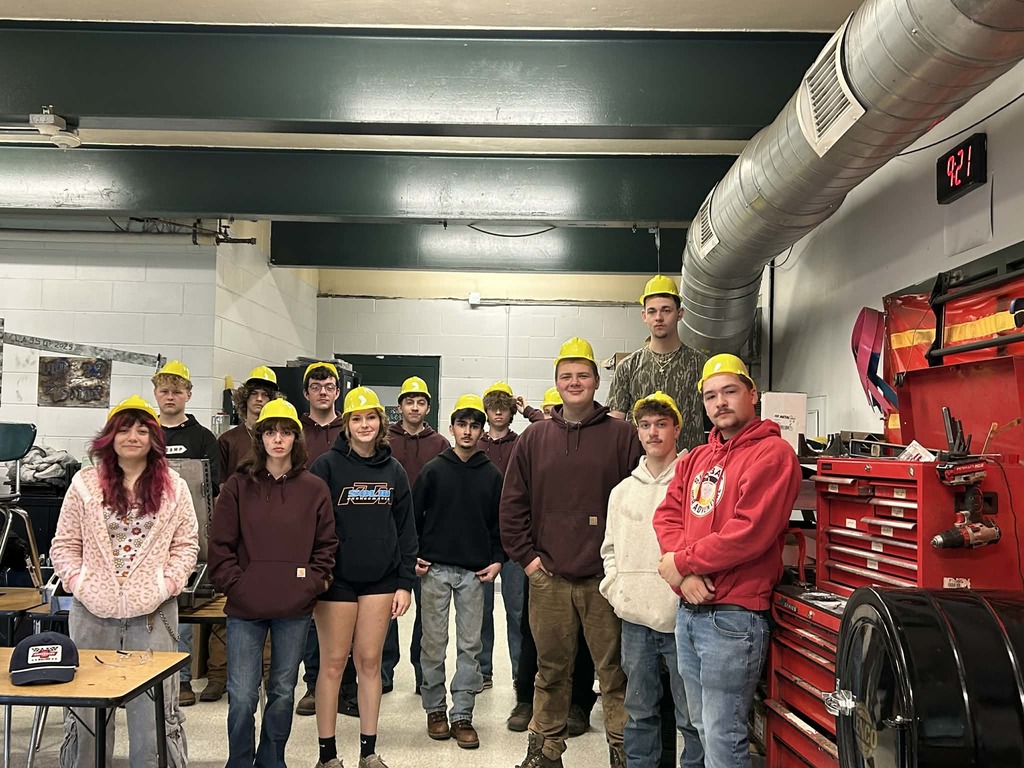 14 high school students in a shop with yellow hard hats on