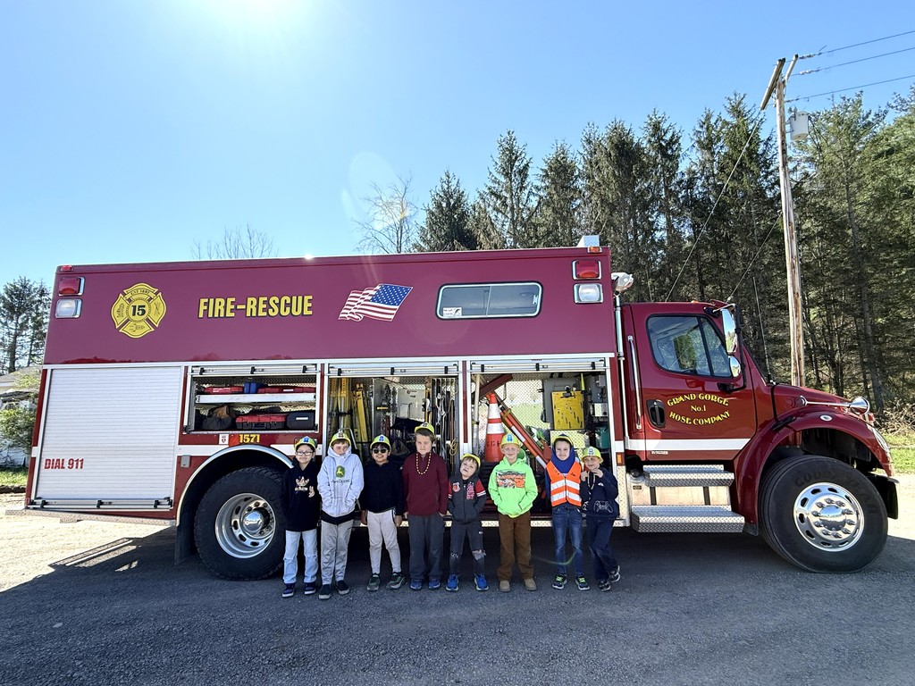 8 elementary students standing in front of the side of the red Grand Gorge red fire-rescue truck with sides of the truck open showing the equipment