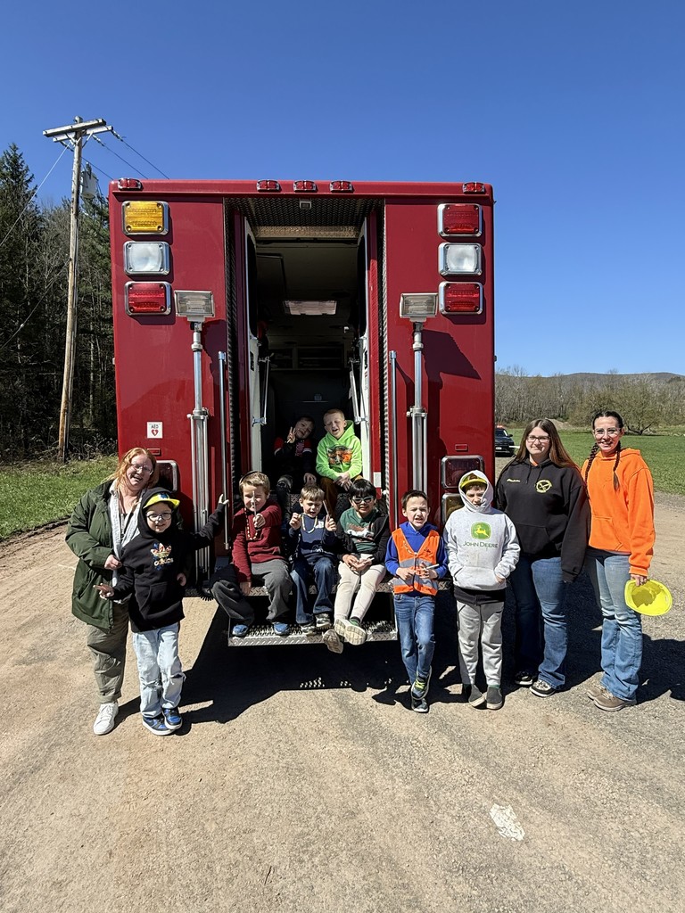 8 elementary students and three staff members standing near and sitting on the back of the fire truck