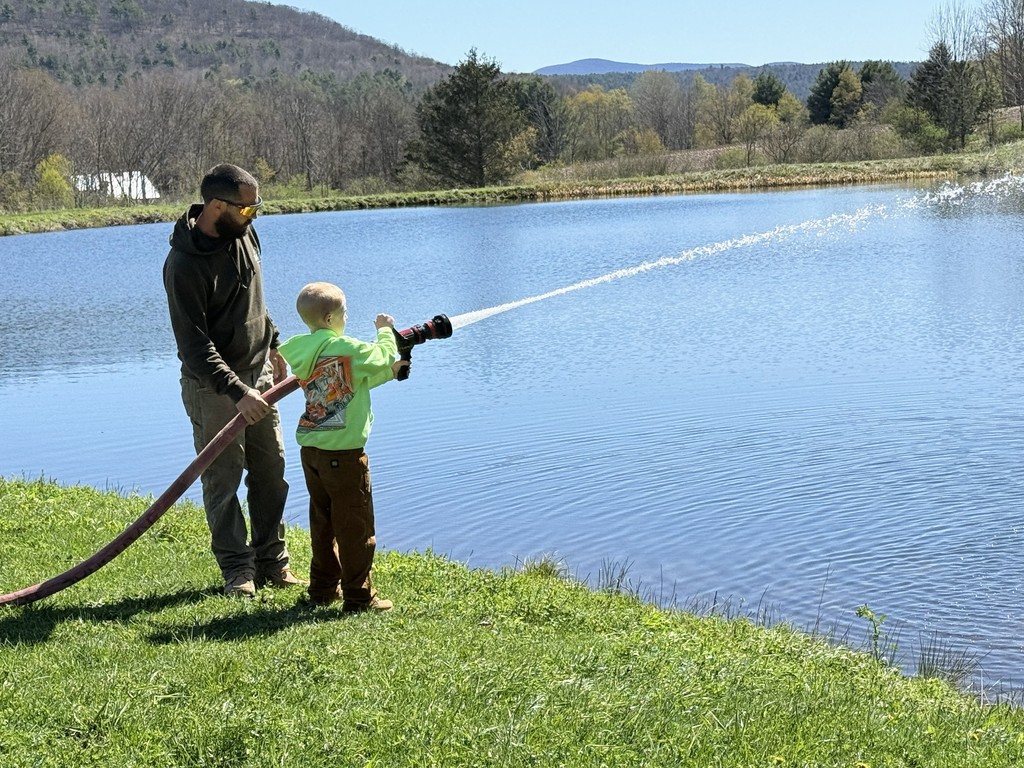 Adult and student holding fire hosing and spraying it into the pond
