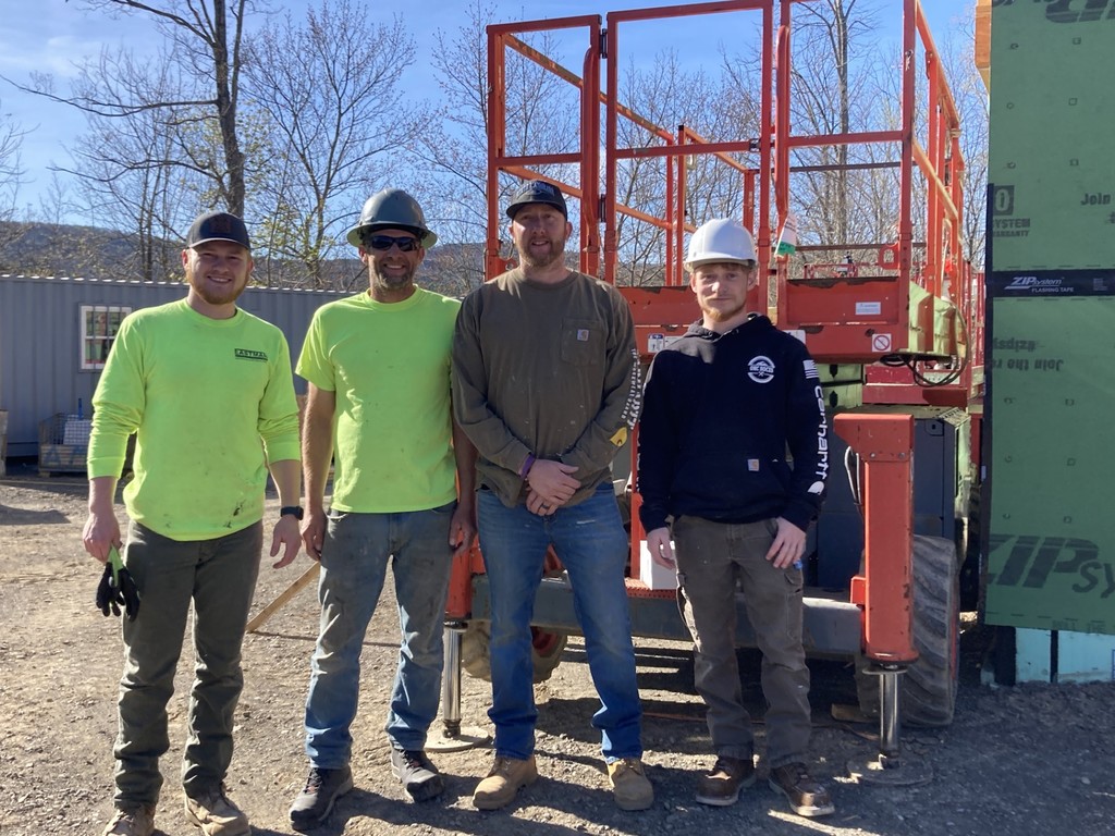 Two Eastman employees, Building Trades instructor, and student posing in front of a lift.