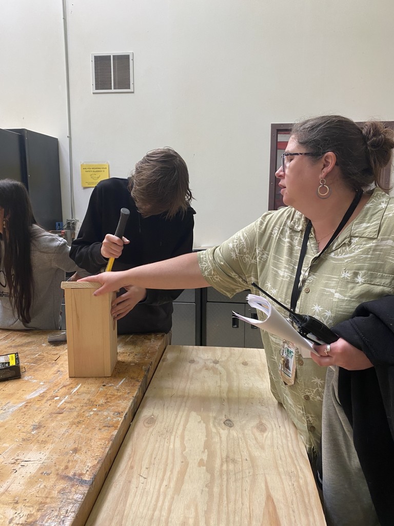 Staff member holding a birdhouse while a student pounds a nail