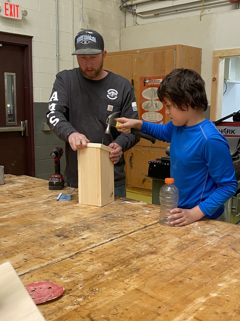 Building Trades instructor holding a birdhouse while a student pounds a nail with a hammer