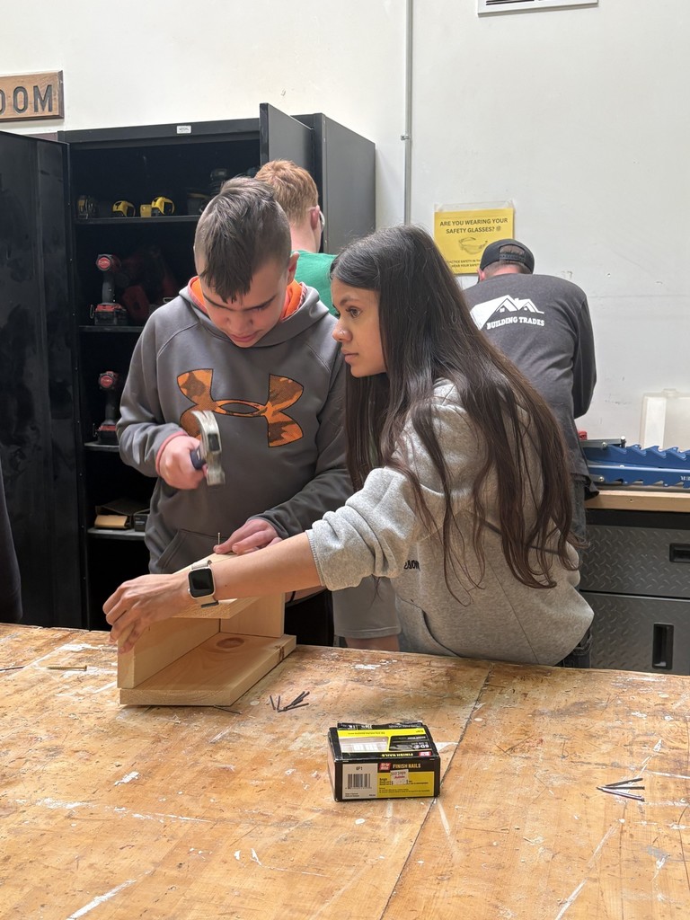 Staff member holding a birdhouse while a student uses a hammer to pound in a nail.
