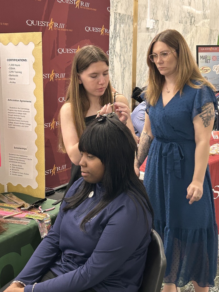 Cosmetology student working on putting tinsel in someone's hair while their instructor looks on.