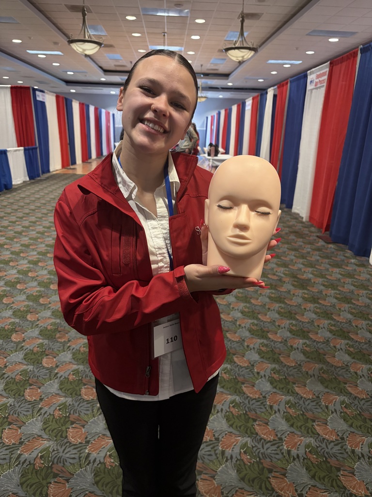 Student wearing a red jacket, white shirt, and black pants holding a mannequin head