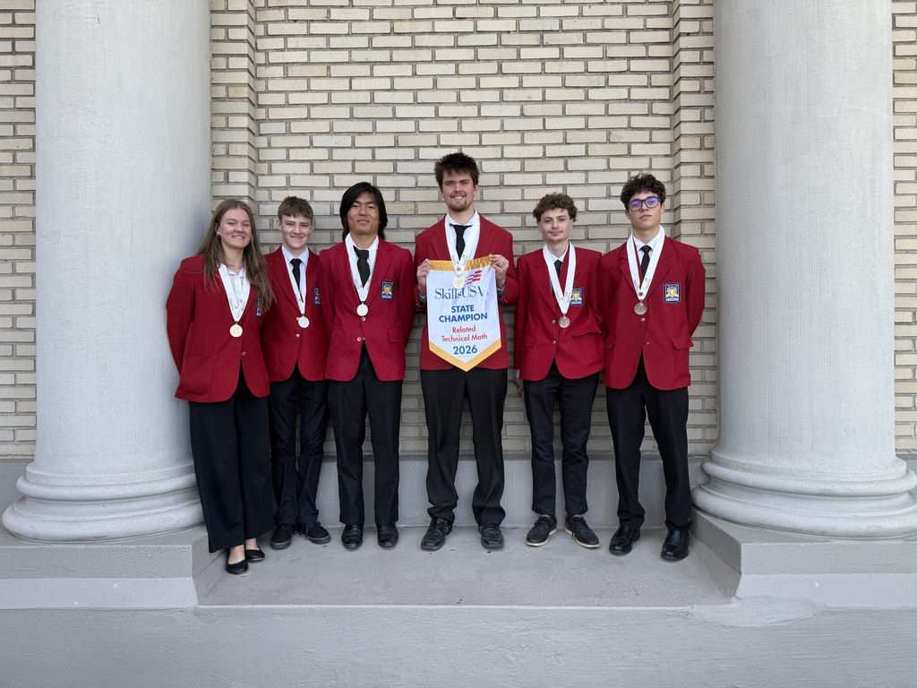 Six students wearing red jackets and black pants with medals. One student is holding a banner that says SkillsUSA State Champion Related Technical Math