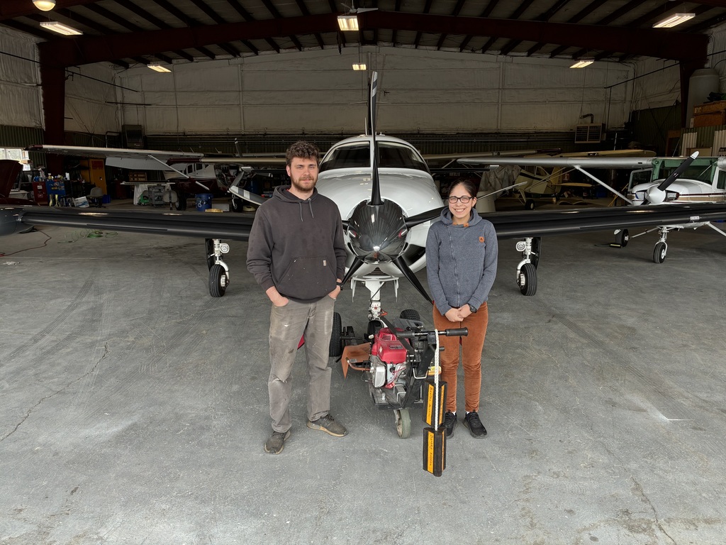 Student and an airport employee standing in front of a small plane.