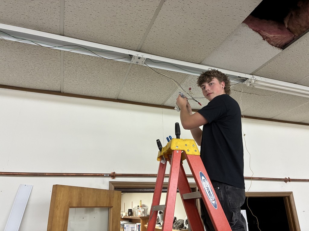 Student standing on a ladder working on lighting on the ceiling.