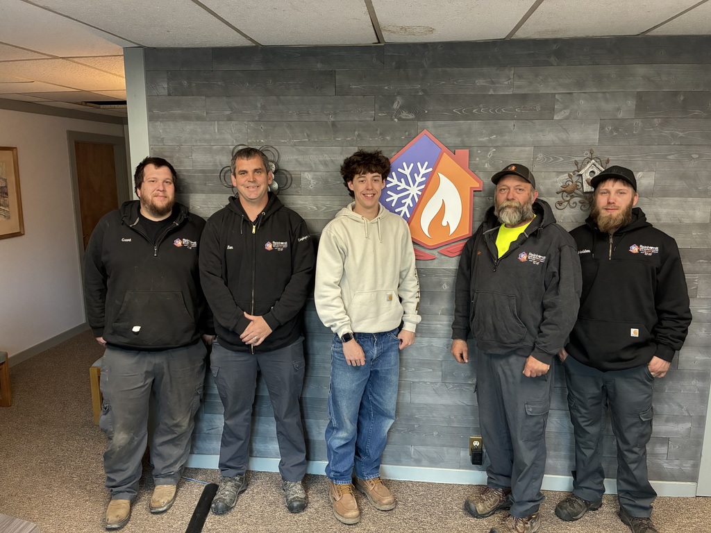 Student and four employees of Reinhardt standing in front of a wall with the Reinhardt logo on it - half snowflake and half flame.