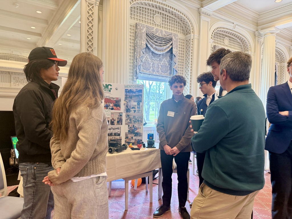 Students gathered around a presentation table speaking with guests