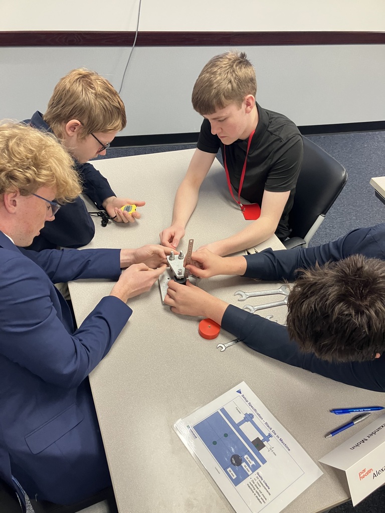 Four students sitting at a table, one with a stopwatch and the others working on solving something with tools.