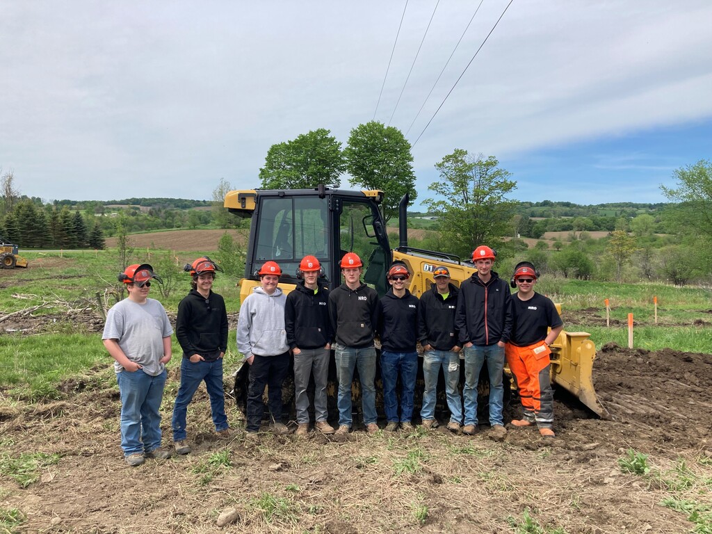9 students wearing hard hats standing in front of a bulldozer.