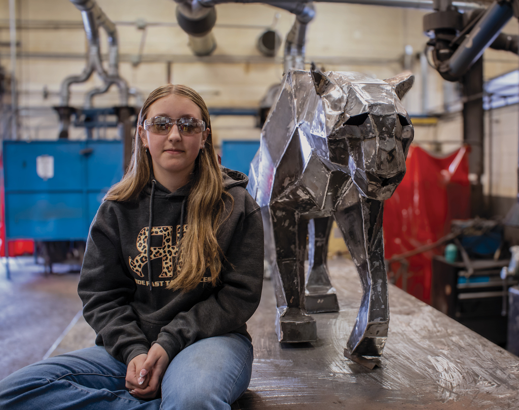 Student sitting next to the welded panther they created with the panther facing the camera.