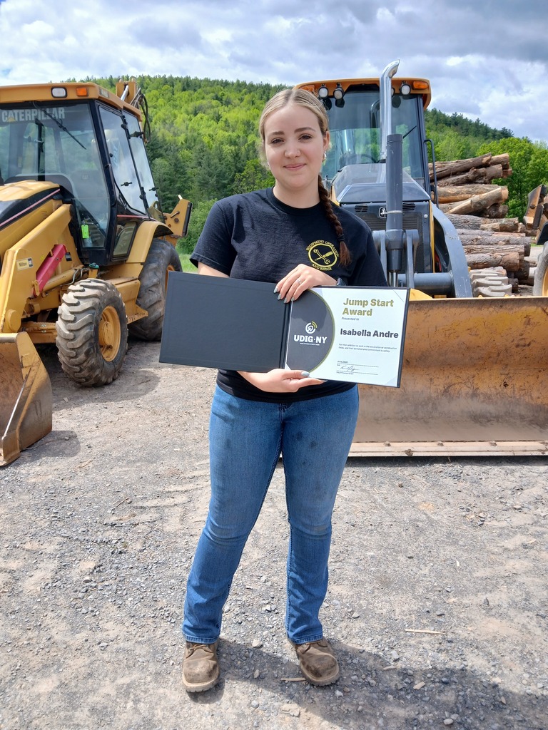 Student standing in front of two bulldozers holding their Jump Start Award