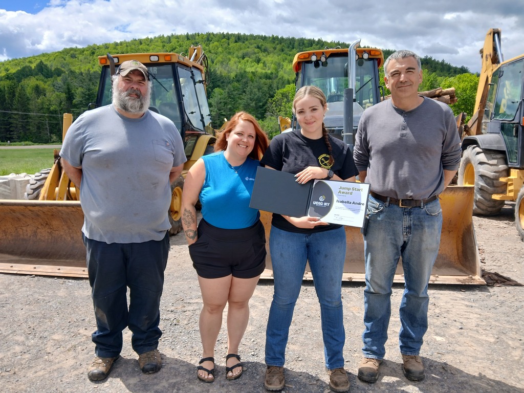 Student, two instructors, and Udig Representative standing in front of two bulldozers.