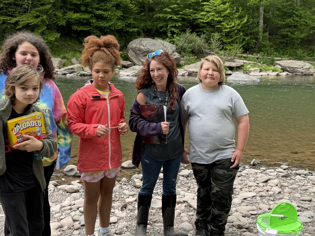 Four students and the teacher standing on the edge of the river posing