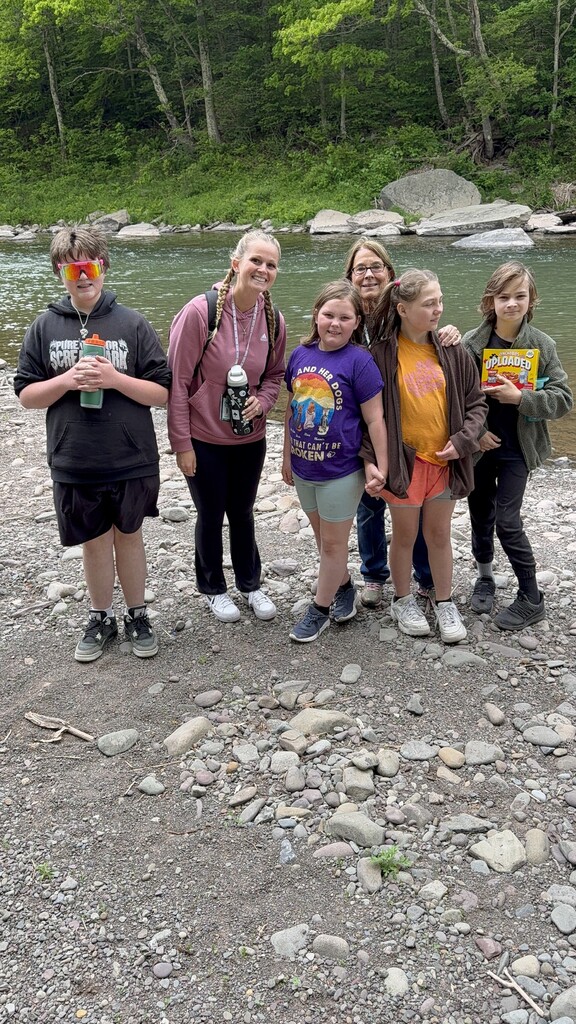 Four students and two staff members standing on the edge of the river posing for a picture