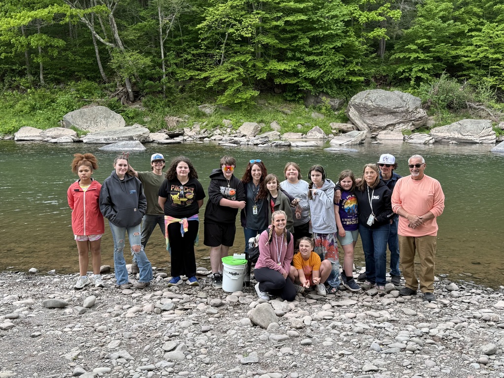 A group photo of students, staff members, and volunteers posing for a picture at the edge of the river bank.