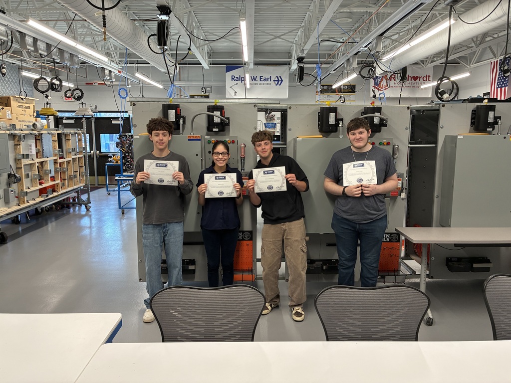 Four students standing in front of mechatronics machinery holding their completion certificates.