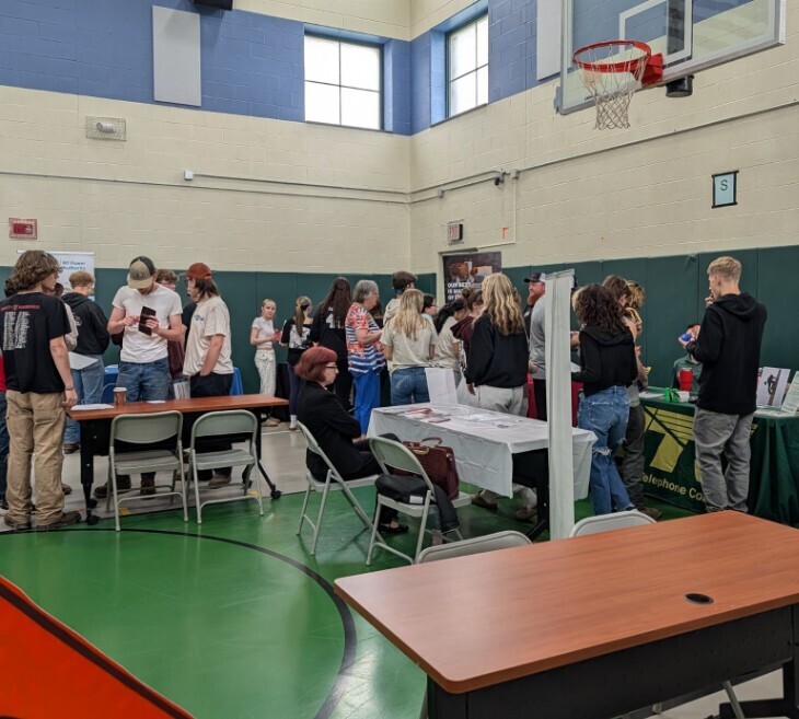 Many students around business tables in a gym.