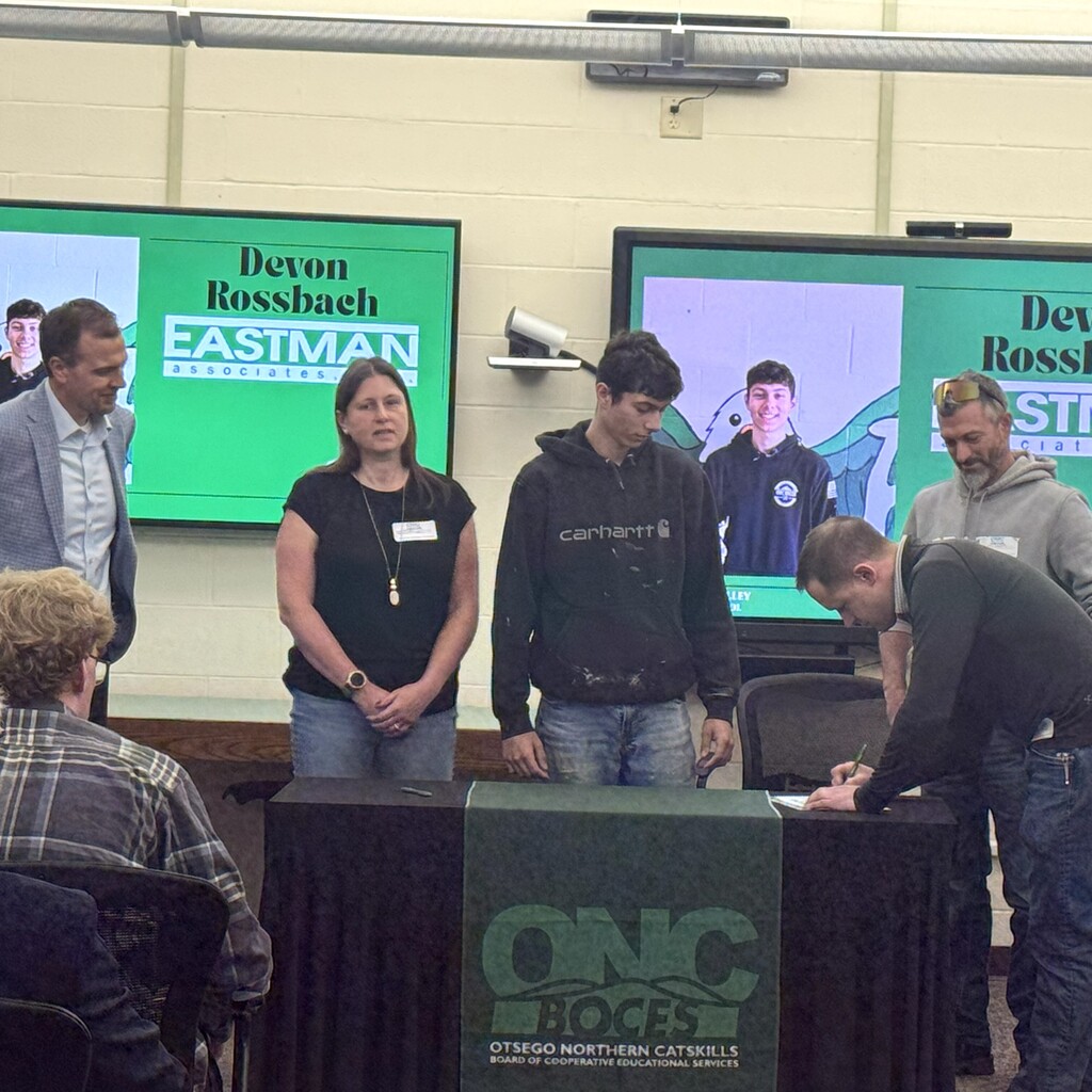 School superintendent, student's parents, and student watching as business representative signs commitment letter