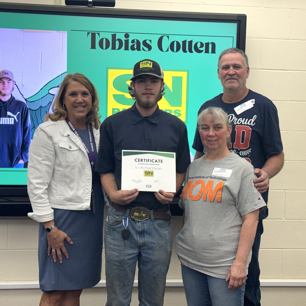 School superintendent, student holding a certificate, and students parents posing for a picture