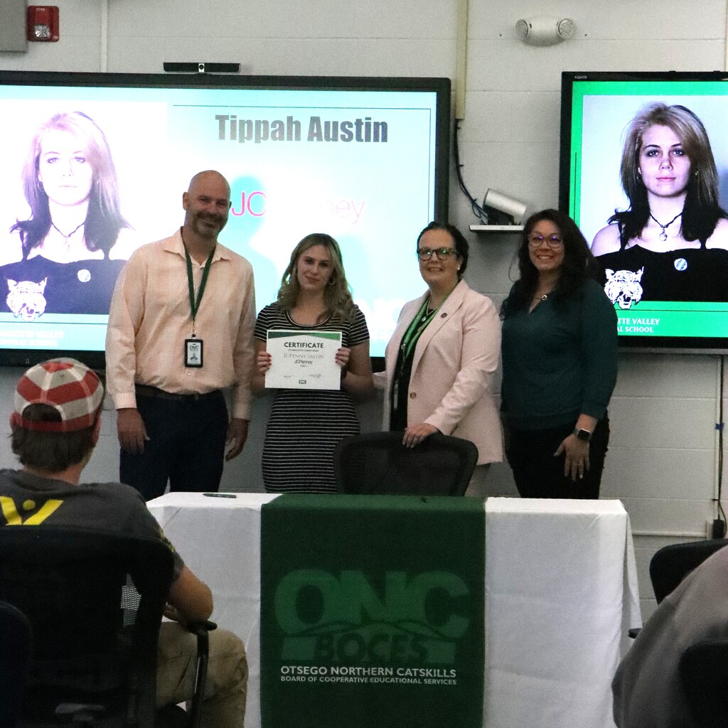 Assistant Superintendent, student, ONC BOCES district superintendent, and school superintendent standing behind a table with a white table cloth and green ONC BOCES banner. The student is holding a certificate.