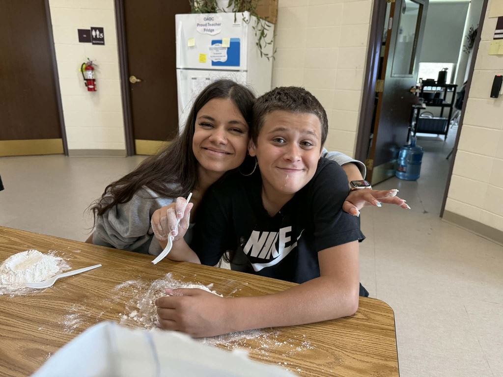 Staff member and student posing for a picture while sitting at a table with pasta dough