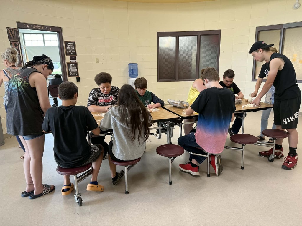 8 students working at a table with pasta dough