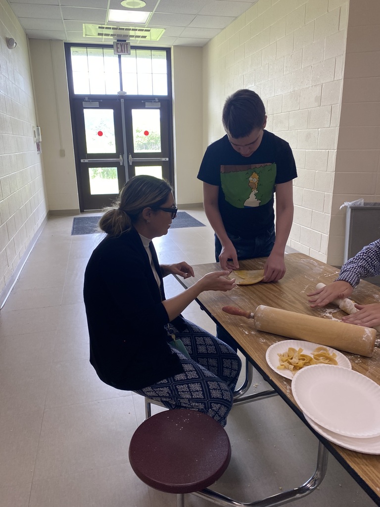 Staff member sitting at a table helping student roll out the dough