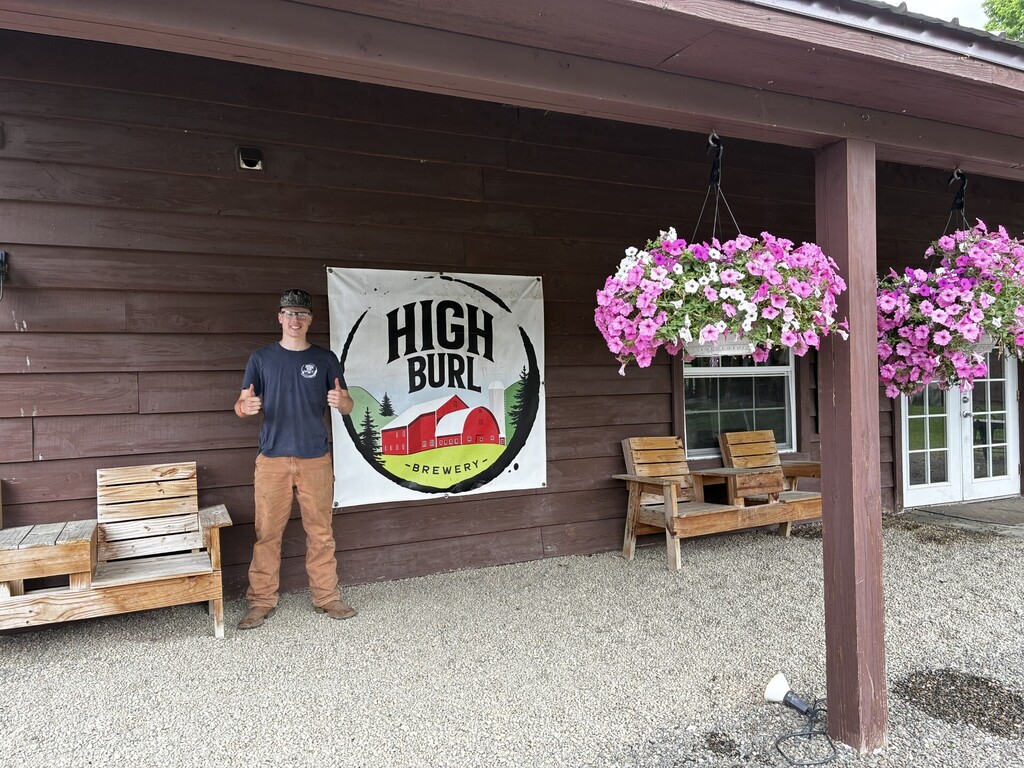 Student standing outside a building next to a sign that says High Burl Brewery.