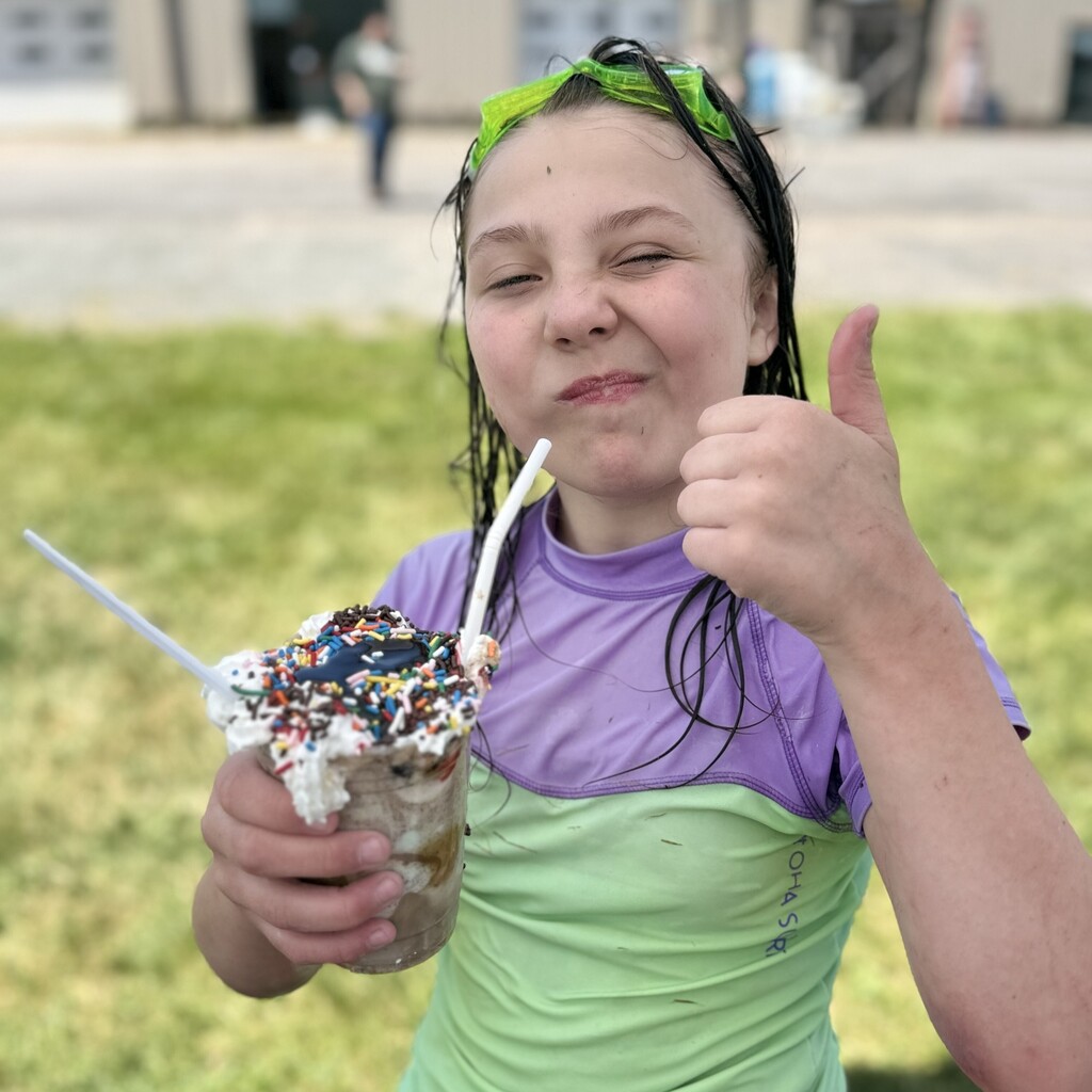 Elementary student wearing swimming goggles on her head giving a thumbs up and holding a root beer float