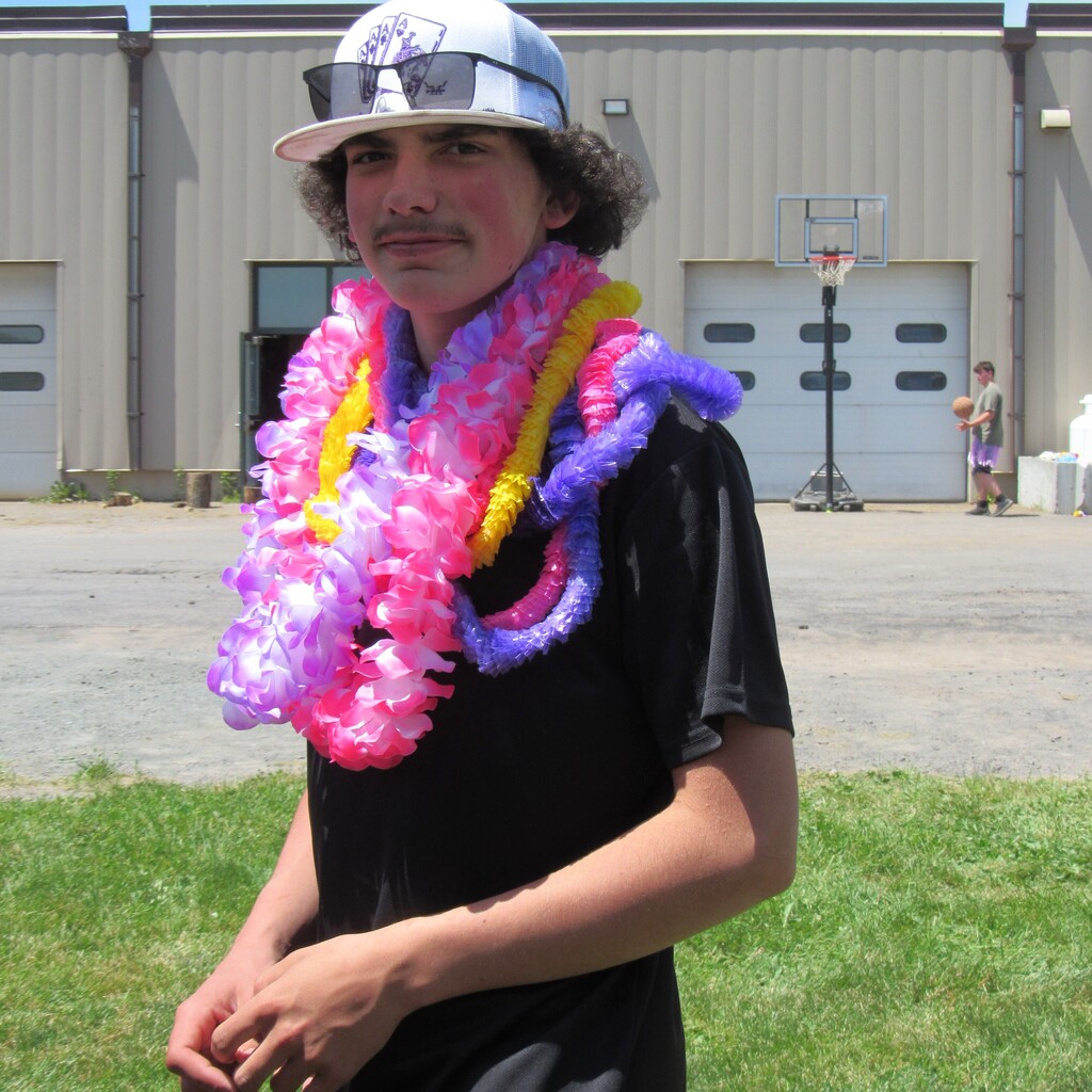 High school student wearing a hat with sunglasses on it and multiple plastic leis around his neck
