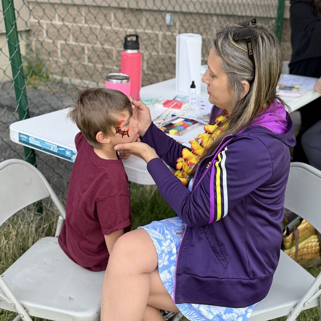 Art teacher sitting and painting an elemntary student's face