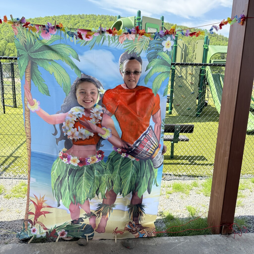 Student and a teacher pose behind a Hawaiian themed photo with the faces cut out so the student and teacher can put their heads through