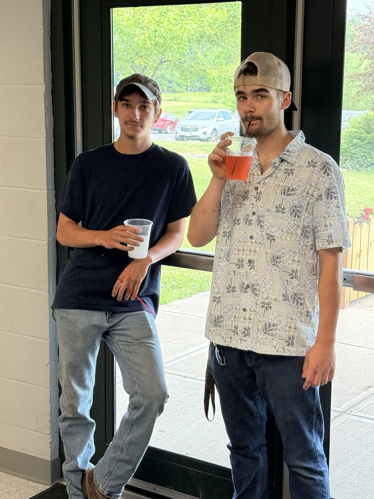 Two high school students wearing hats standing near the door. One is holding a cup and the other is sipping from their straw