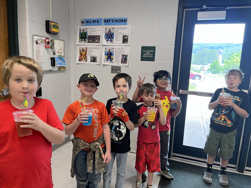6 elementary students in a line in the hallway with cups and straws.
