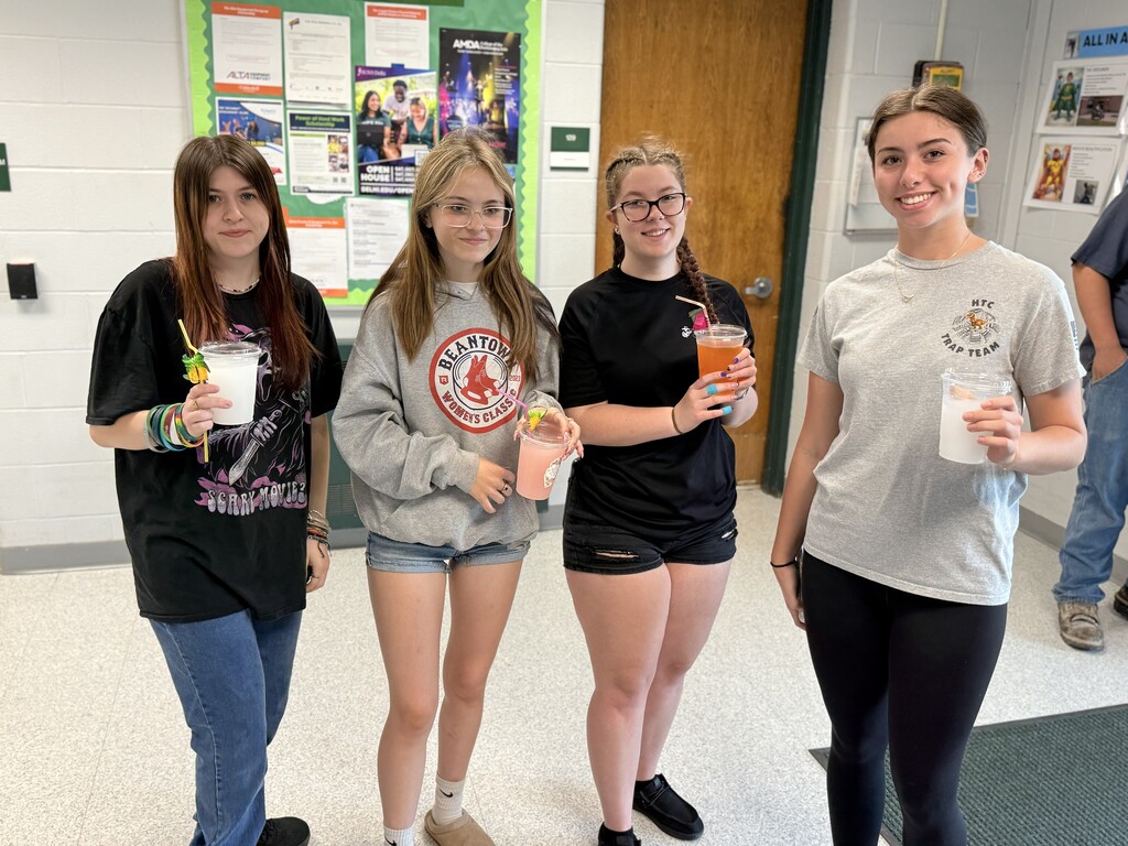 Four high school students posing in a hallway with their cups and straws