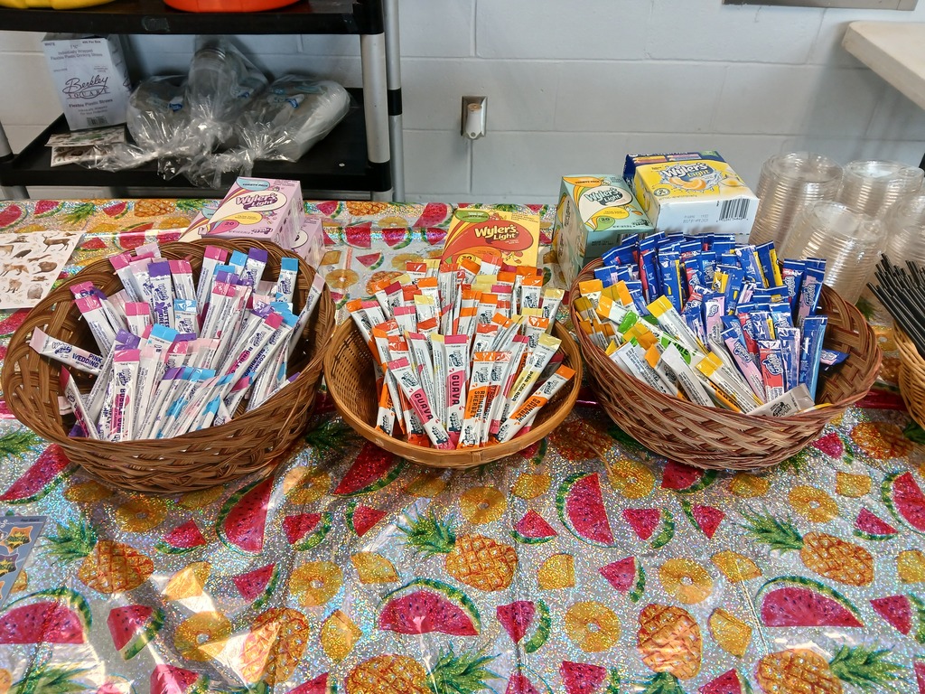 Three baskets on a table with a pineapple and watermelon tablecloth. The baskets have flavored water packts in them.