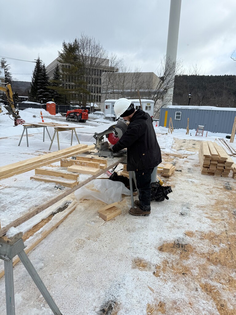 Student working outside using a saw to cut lumber