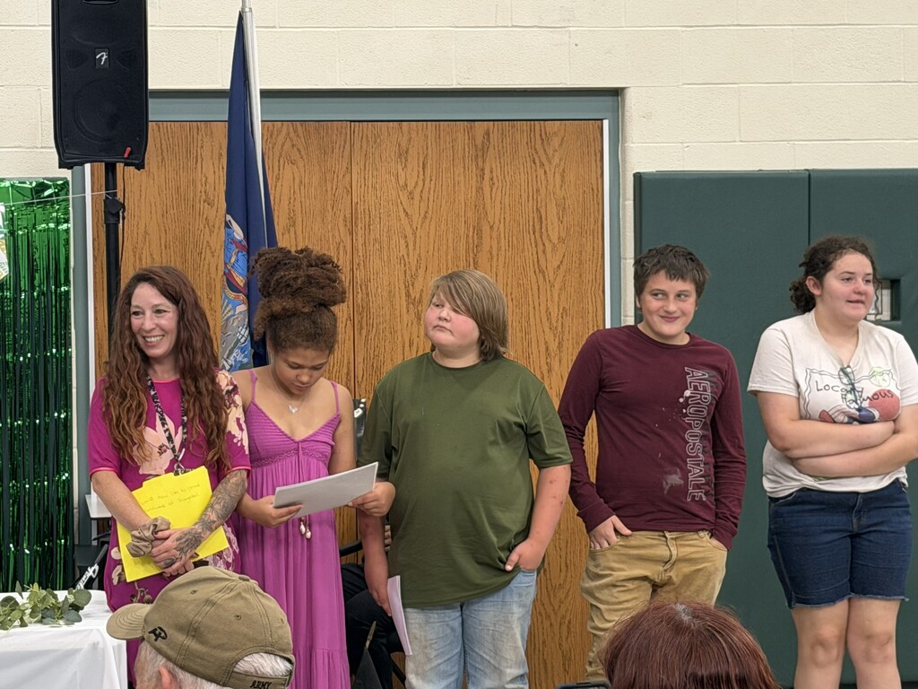 4 middle school students and their teacher standing and listening to a speaker