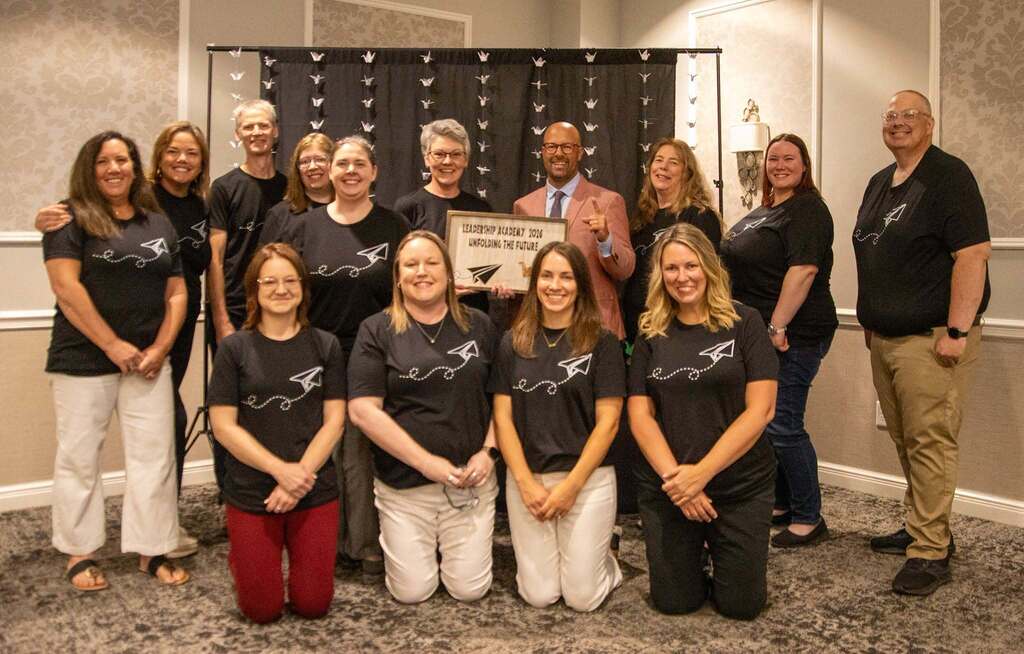 13 people posing for a picture with the keynote speaker.