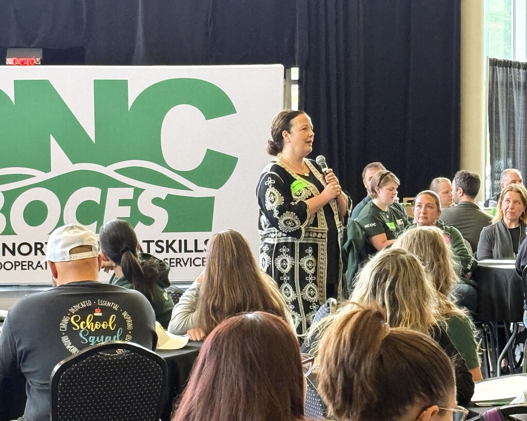 District Superintendent standing among people sitting at tables speaking with a large white and green ONC BOCES banner.