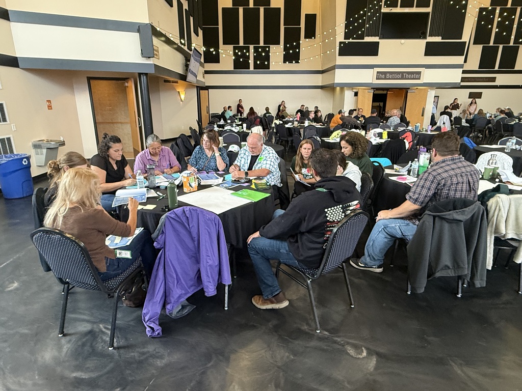 Large group of people sitting in smaller groups at tables talking.