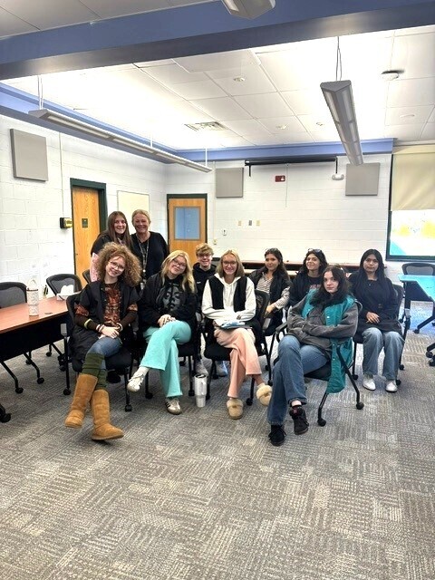 9 cosmetology students and the instructor posing for a picture in a conference room