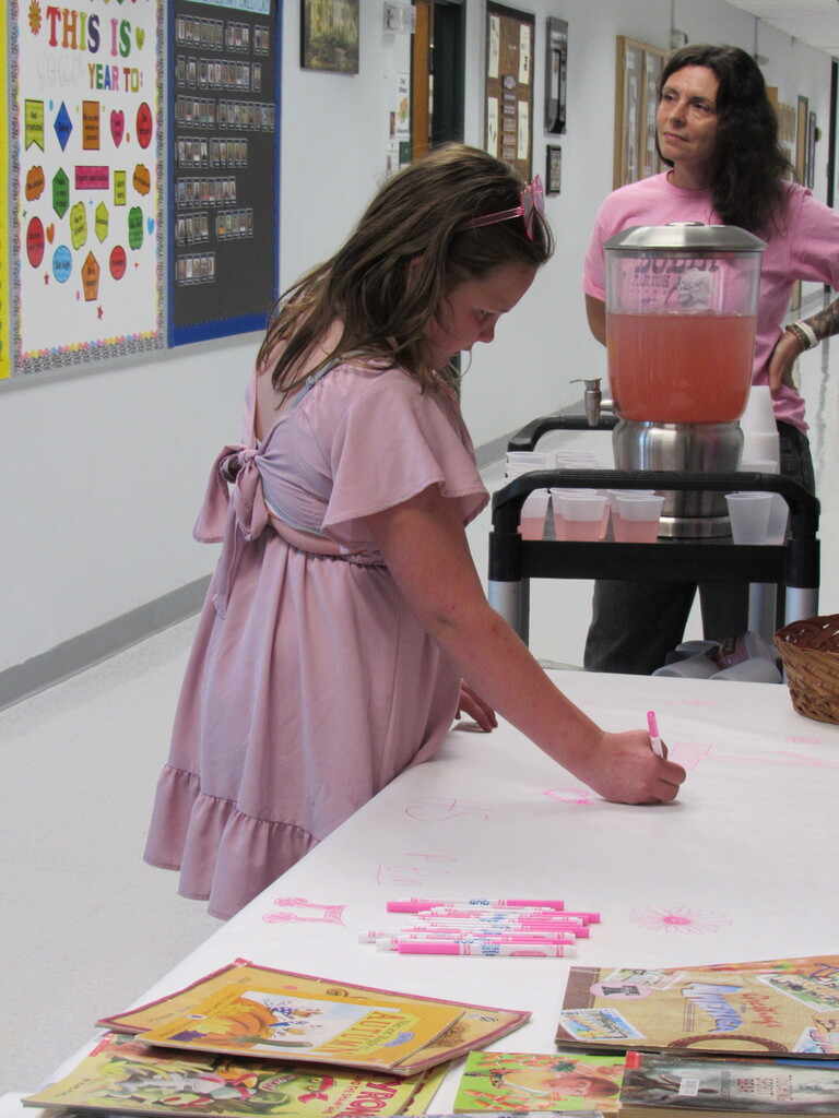 Girl in pink dress standing next to lemonade container with a staff member